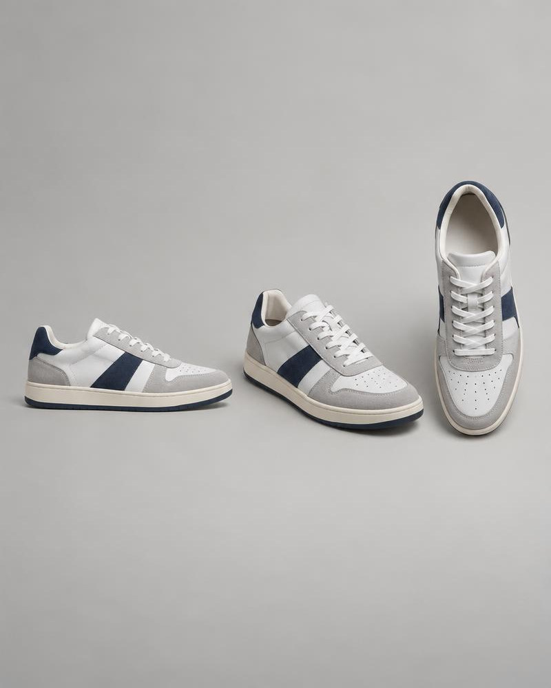White and navy low-top sneaker photographed from the side, front angle, and above on gray.